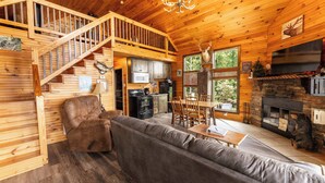 A wooden cabin interior with a staircase, living room, dining area, kitchen, and fireplace. - Elk Ridge Cabin – Private Hot Tub & Stunning Views (Bryant)