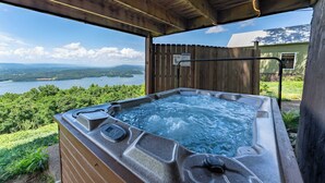 A hot tub with a digital control panel, surrounded by a wooden deck with a view of a lake and mountains.