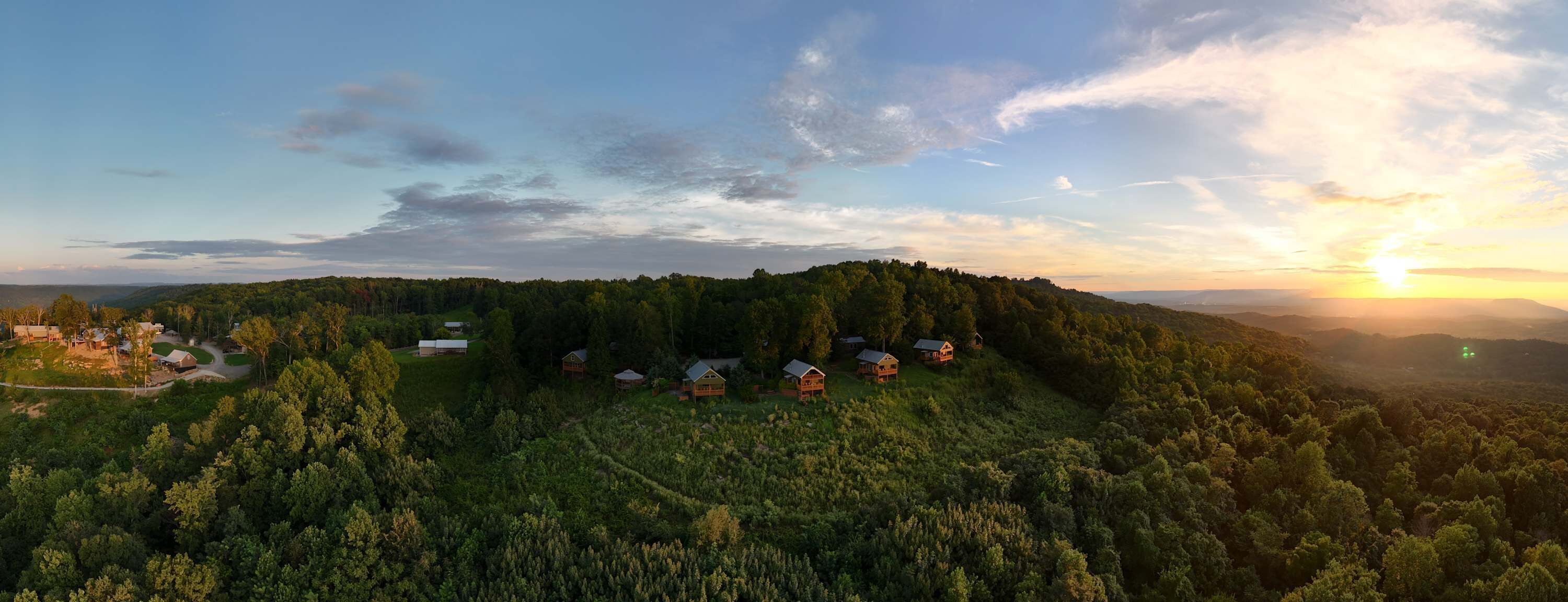 Un área boscosa con varias cabañas y un edificio grande, probablemente un albergue o resort, rodeado de árboles frondosos y colinas.