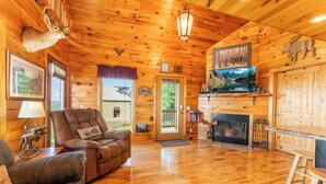 A cozy cabin interior with wooden walls, a fireplace, a mounted deer head, and a television.