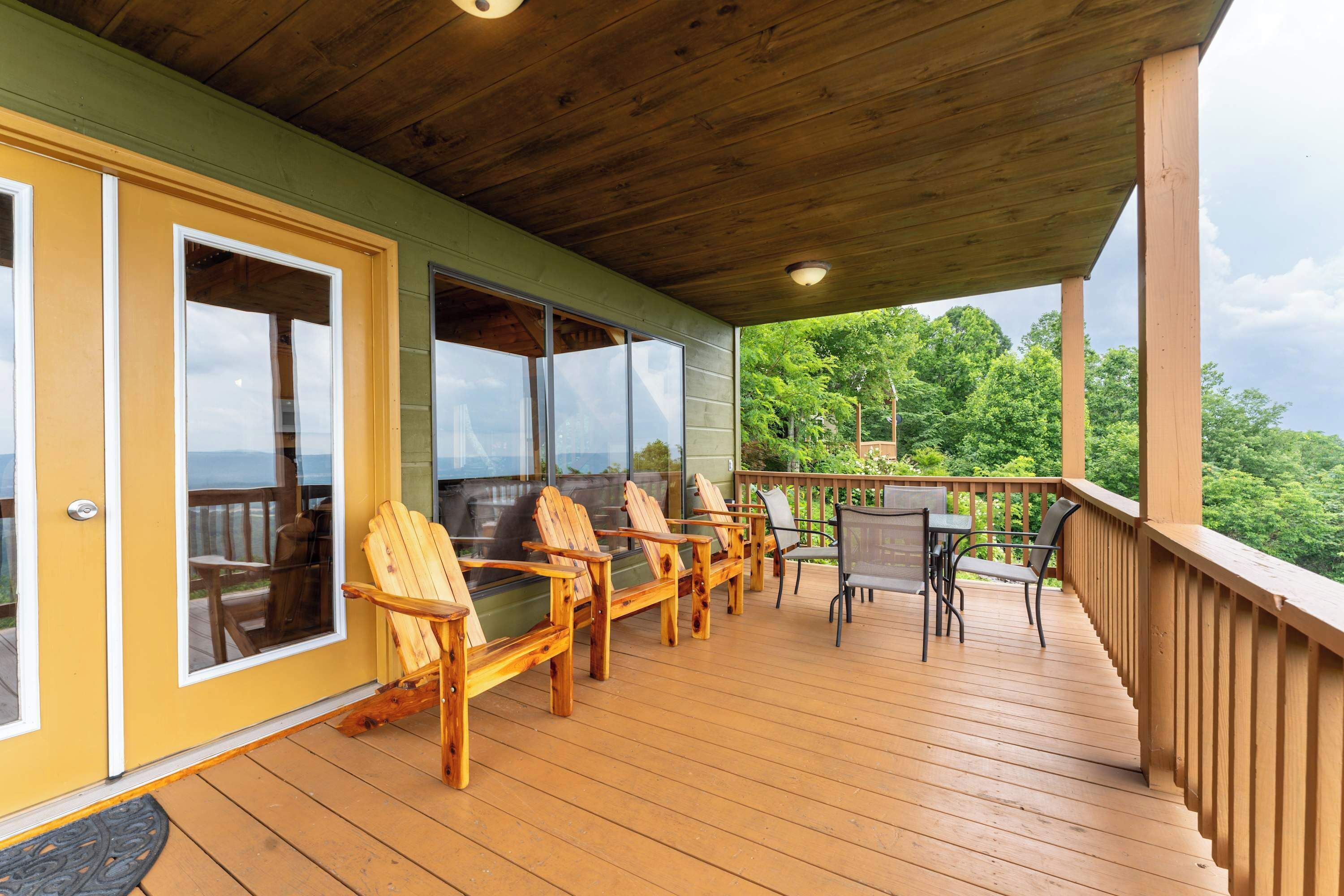 Un terrazzo in legno con poltrone Adirondack e un tavolo, affacciato su un panorama.