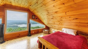 Une pièce de cabane en bois avec une grande fenêtre, un lit et un radiateur.