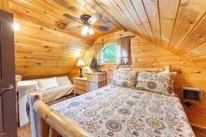 Une chambre confortable, aménagée dans un chalet en bois, avec un lit, des tables de chevet, une fenêtre et un ventilateur de plafond.