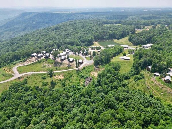 An aerial view of a campground with several RVs and cabins spread across a hilly terrain with dense forest.