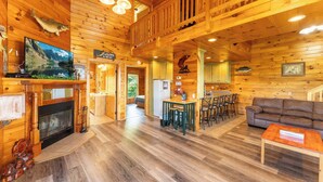 L’intérieur d’un chalet en bois comprend une cheminée, un téléviseur, un coin repas et un canapé.