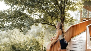 Une femme se tient sur un pont en bois muni de garde-corps, entourée de verdure.