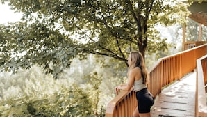 A woman standing on a wooden bridge with railings, surrounded by greenery. - Turkey Hollow cabin with a private hot tub! (Bryant)