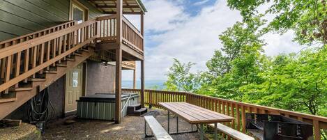 Una terraza de madera con una mesa de picnic y bancos, un jacuzzi y una escalera que lleva a una zona cubierta.