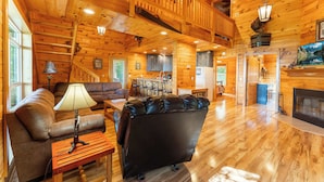 A spacious living room with a leather sofa, a wooden coffee table, and a fireplace. - Turkey Hollow cabin with a private hot tub! (Bryant)