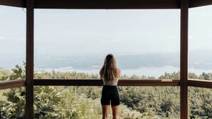 A person standing on a balcony with a view of a lake and surrounding greenery. - Turkey Hollow cabin with a private hot tub! (Bryant)