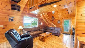 A wooden cabin interior with a leather recliner, a wooden coffee table, and a staircase leading to an upper level. - Turkey Hollow cabin with a private hot tub! (Bryant)