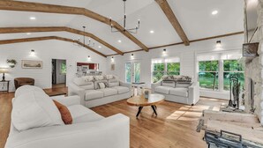 A spacious living room with white sofas, a wooden coffee table, and exposed wooden beams on the ceiling. - Hummingbird Cabin with a private hot tub! (Bryant)