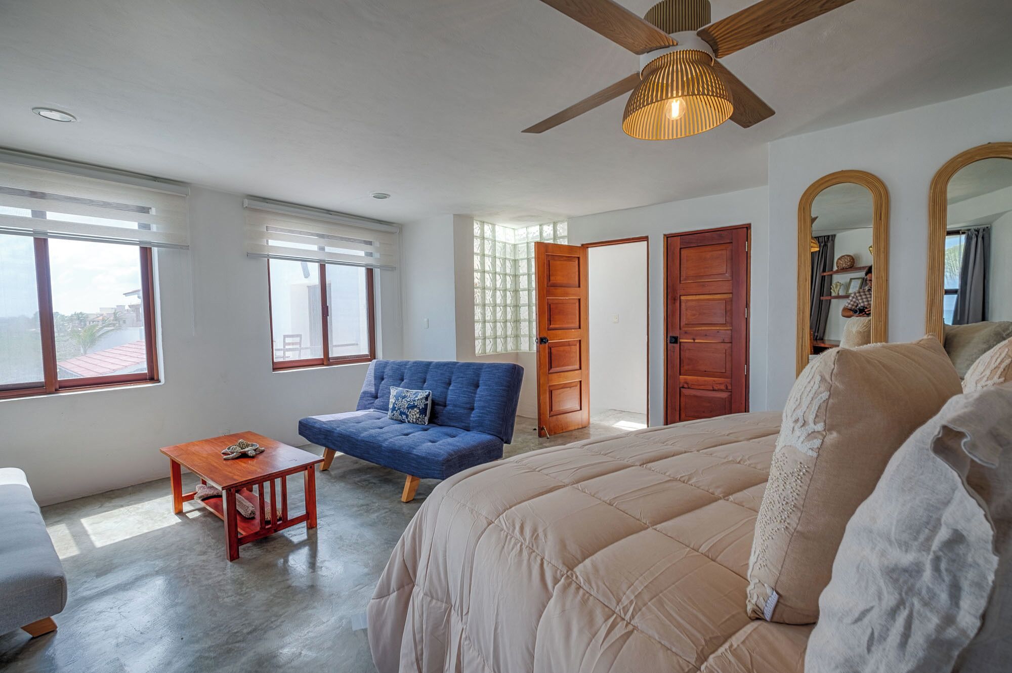 A bedroom with a large bed, a blue armchair, a wooden table, and a ceiling fan.