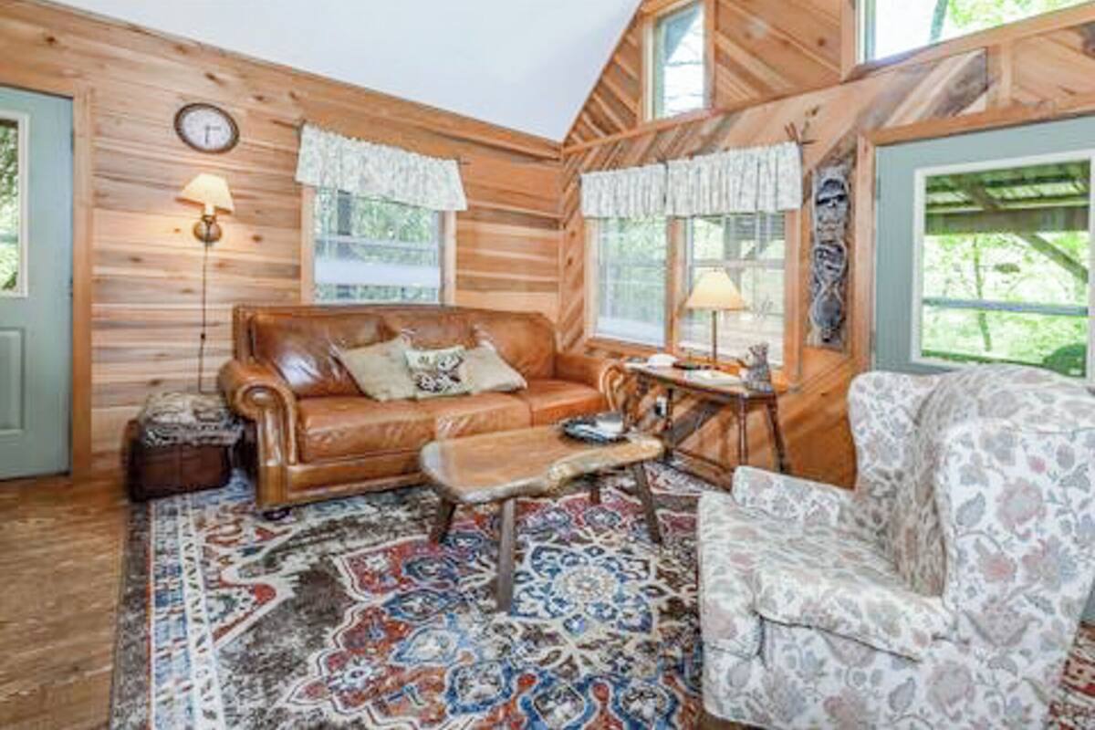 A cozy cabin interior with a wooden interior, a leather sofa, a patterned rug, and a small table with a lamp.