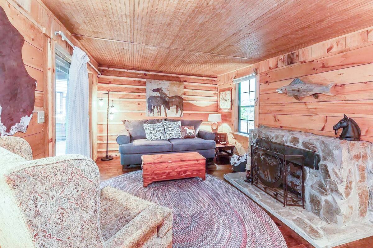 A log cabin interior with a fireplace, a sofa, a patterned armchair, and a rug.