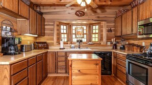 A rustic kitchen with wooden cabinets, a central island, a stove, and a microwave. - The Cabins at Seven Foxes (Lake Toxaway)