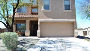 A two-story house with a garage, a covered porch, and a small front yard with a bush. - Tucson Sonoran Desert Retreat! (Tucson)