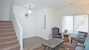 A spacious living room with a staircase, a large window with blinds, a leather armchair, a patterned coffee table, and a small side table. - Tucson Sonoran Desert Retreat! (Tucson)
