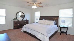 A bedroom with a bed, dresser, mirror, ceiling fan, and windows. - Tucson Sonoran Desert Retreat! (Tucson)