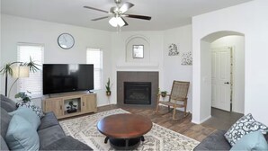 A living room with a TV, sofa, coffee table, fireplace, and a ceiling fan. - Tucson Sonoran Desert Retreat! (Tucson)