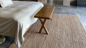 Un dormitorio moderno con una cama grande, un banco de madera y una pared de concreto decorativa.