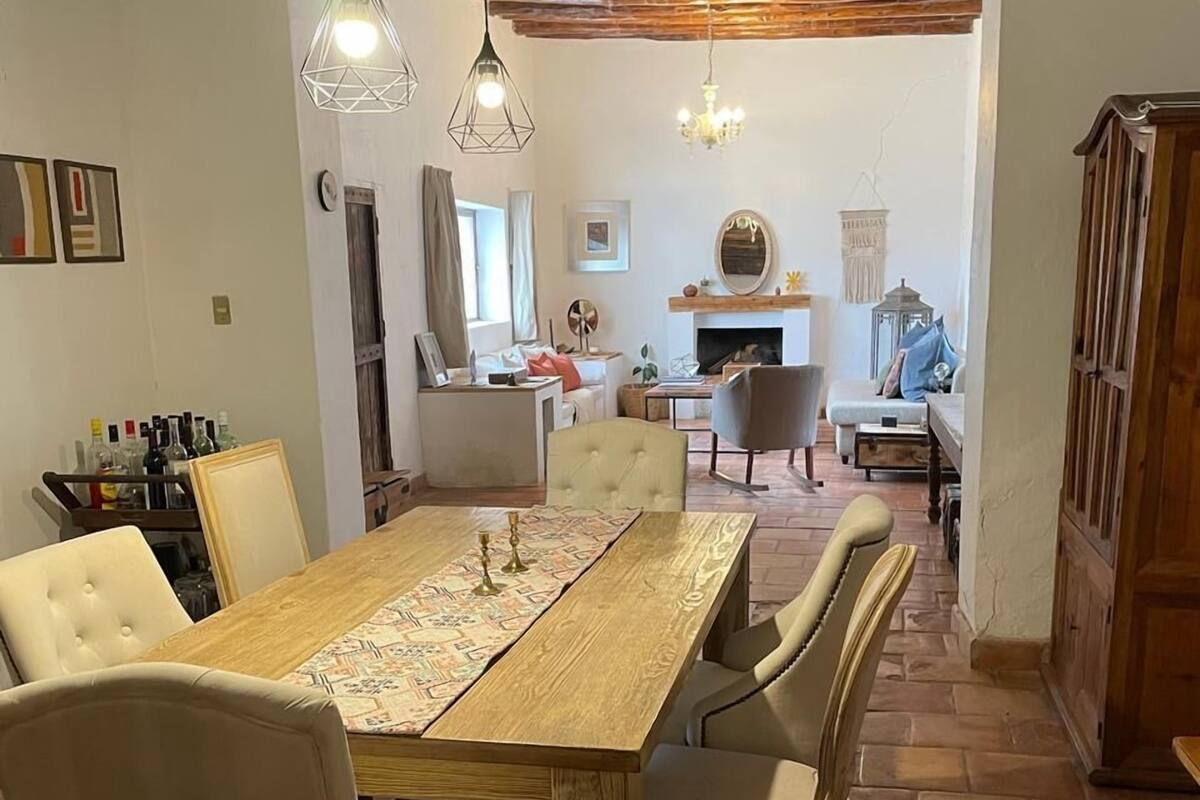 A dining area with a wooden table, white upholstered chairs, and hanging pendant lights.