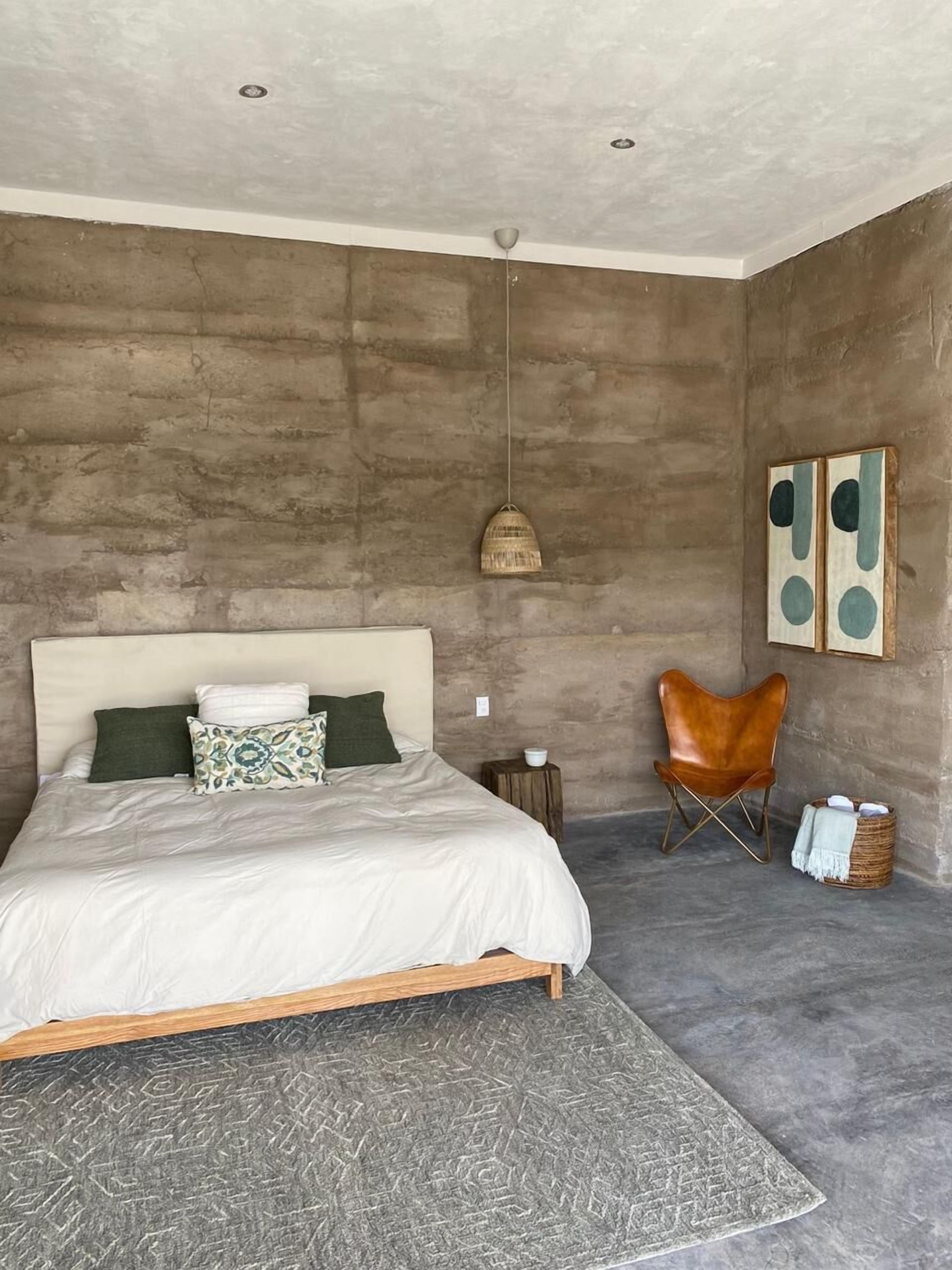 A bedroom with a large bed, a hanging light, a chair, and artwork on the wall.