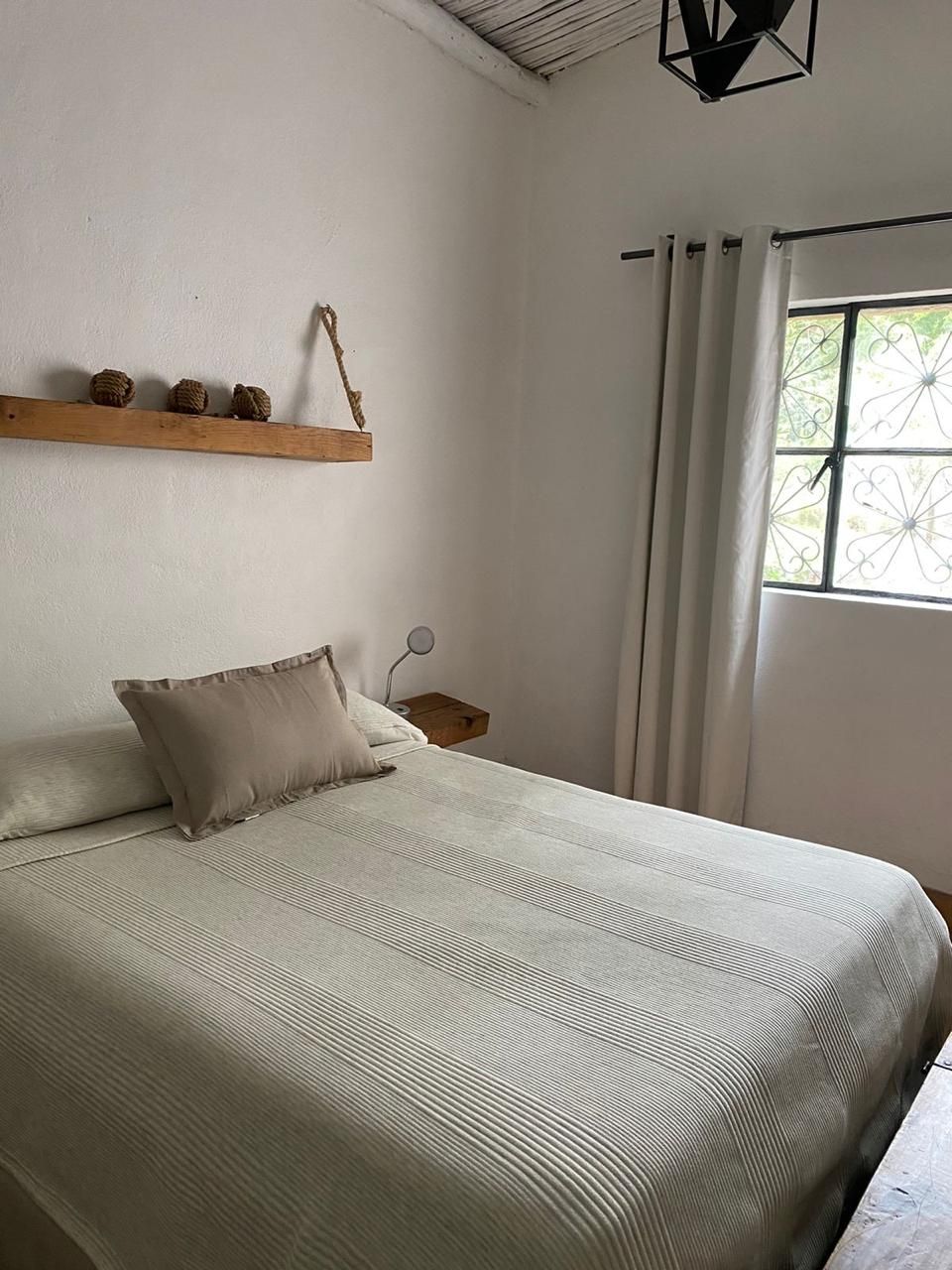 A neatly made bed with a striped bedspread, a bedside table with a lamp, and a window with curtains.