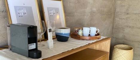 Une commode en bois, recouverte d’un tissu blanc, sur laquelle sont posés une machine à café, un verre et une tasse.