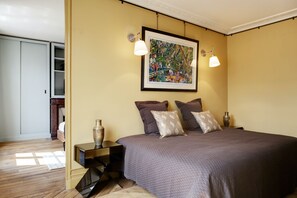 A bedroom with a bed, bedside lamps, a nightstand, a decorative vase, and a framed painting on the wall.