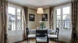 Un comedor con una mesa redonda, cuatro sillas, un jarrón con flores y dos cuadros con motivos florales en la pared.