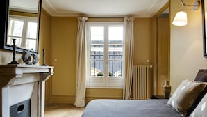 Un dormitorio con cama, ventana con cortinas, radiador y mesita de noche con lámpara.
