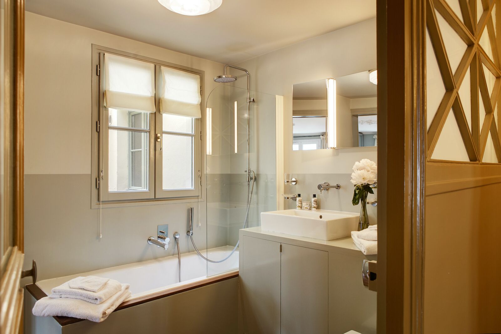 A modern bathroom with a bathtub, a glass-enclosed shower, a vanity with a mirror, and a window with blinds.