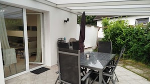 A patio area with a table and chairs, a sliding glass door, and a covered seating area. - Vacation Apartment (GF) at Grossensee - Relaxation Close to Hamburg (großensee)