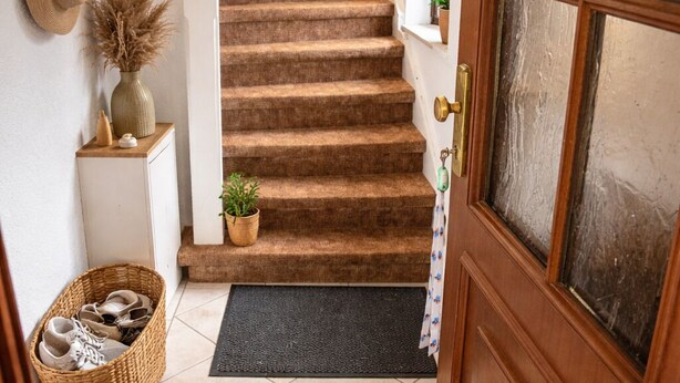 A staircase leading to a second floor, a wooden door with a glass panel, a welcome mat, a basket with shoes, and a wall-mounted mirror. - Cozy Attic Apartment on Großensee - Relaxation at the Gates of Hamburg (Grossensee)