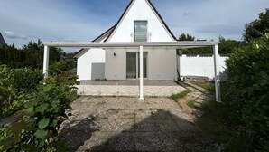 A modern house with a white exterior, a sloped roof, and a covered patio area. - Cozy Attic Apartment on Großensee - Relaxation at the Gates of Hamburg (Grossensee)