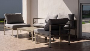 Un área de estar moderna al aire libre con dos sofás y una mesita, ubicada cerca de un ventanal grande.