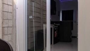 Una habitación con puerta de vidrio corrediza que da a un balcón, zona de cocina con armarios y microondas, y un refrigerador de color oscuro.