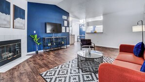 Un salon moderne avec une cheminée, un téléviseur fixé au mur, un coin repas et un canapé rouge.