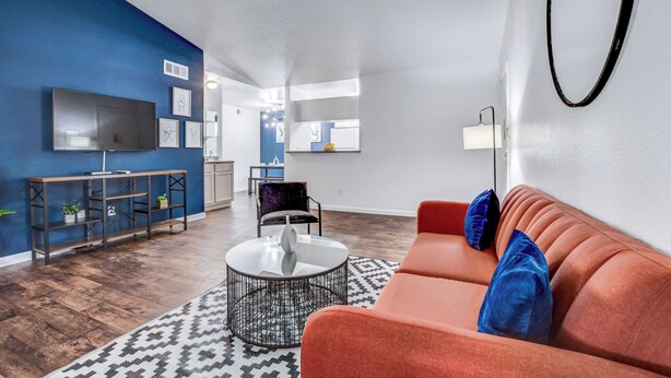 Un salon moderne avec un mur d’accent bleu, un téléviseur à écran plat, une table basse ronde et un canapé rouge agrémenté de coussins bleus.