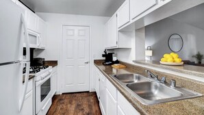 Une cuisine moderne avec des meubles blancs, un plan de travail en granit, des éviers en acier inoxydable et un plancher en bois.
