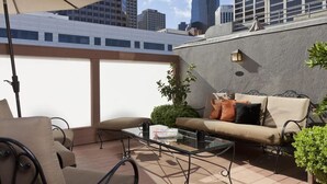Una terraza en la azotea con una mesa de vidrio, sofá color beige y sillas exteriores.