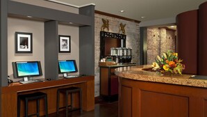 Un vestíbulo de hotel con una mesa de recepción, dos monitores, una cafetera y un arreglo floral.