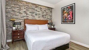 A bedroom with a brick-patterned wall, a wooden headboard, a large bed with white linens, two bedside tables with lamps, and a framed painting on the wall. - European-Style Suite Steps from Embarcadero with Bay Views in San Francisco (San Francisco)