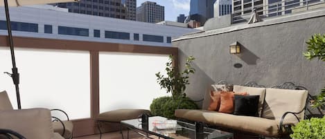 A rooftop patio with a glass table, beige sofa, and outdoor chairs.
