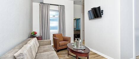 Ein modernes Wohnzimmer mit Sofa, Sessel und Couchtisch. Ein Flachbildfernseher ist an der Wand befestigt.