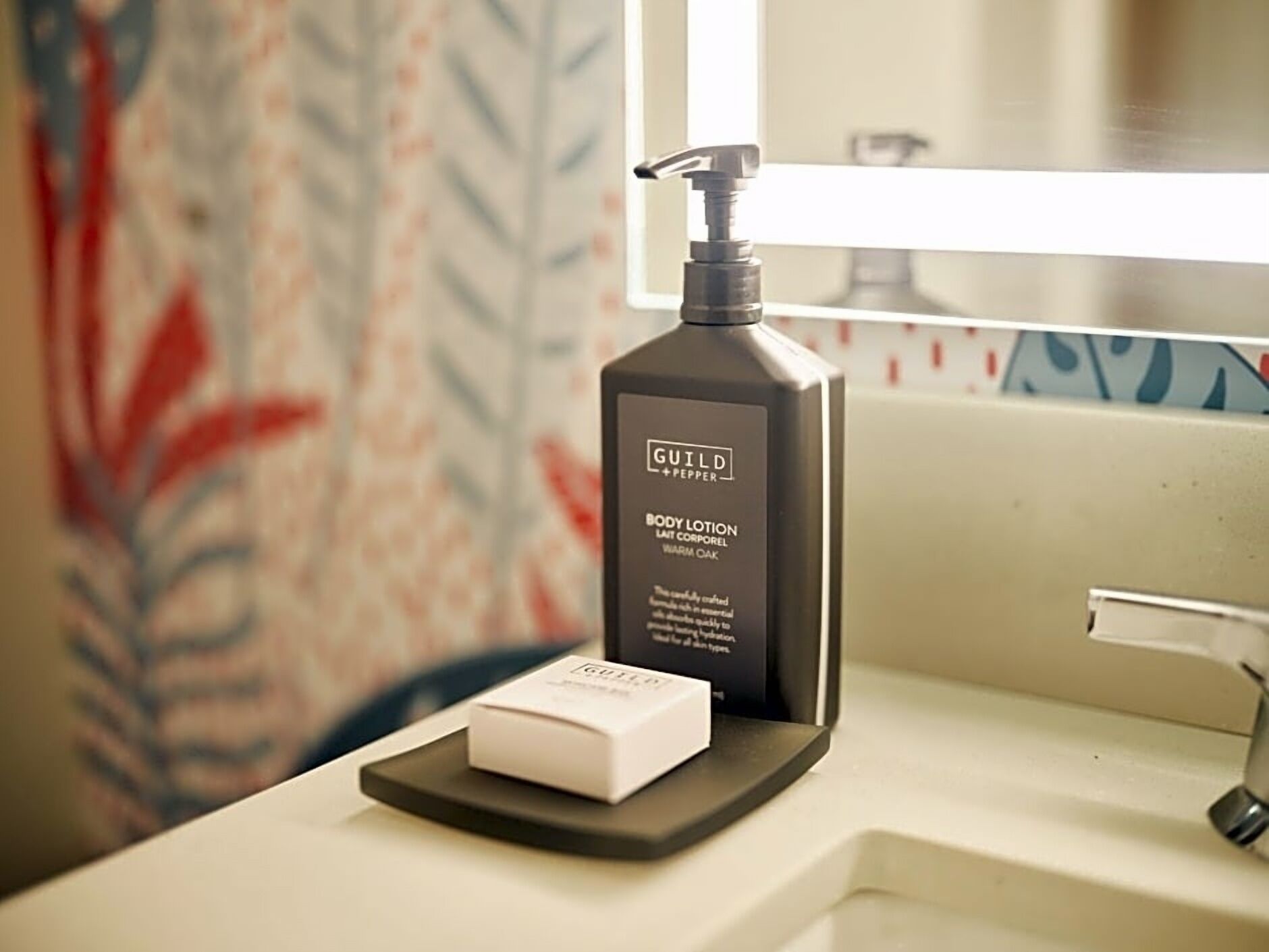 A bathroom with a black bottle of Guild + Pepper body lotion and a white soap bar on a black tray.