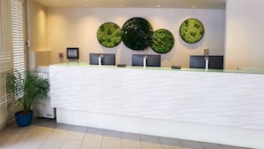 En receptionsdisk med tre bildskärmar, ett stort, grönt konstverk på väggen och en krukväxt.