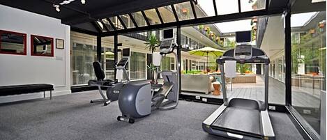 Un gimnasio moderno con equipo cardiovascular, una banca y ventanas amplias que ofrecen vistas al exterior.