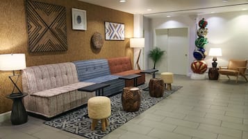 Um lobby moderno com um sofá, pufes e uma mesa de centro. Há obras de arte nas paredes e uma planta decorativa.